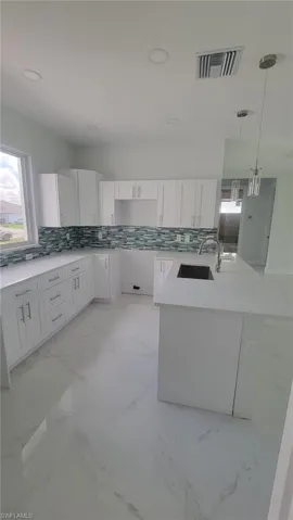 Kitchen featuring pendant lighting, light tile patterned flooring, white cabinets, and decorative backsplash
