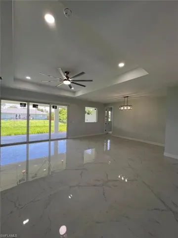 Tiled empty room with ceiling fan and a tray ceiling