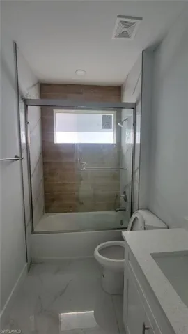 Full bathroom with a wealth of natural light, tile patterned floors, bath / shower combo with glass door, and toilet