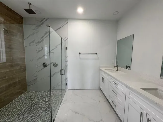 Bathroom featuring tile patterned flooring, a shower with door, and dual bowl vanity