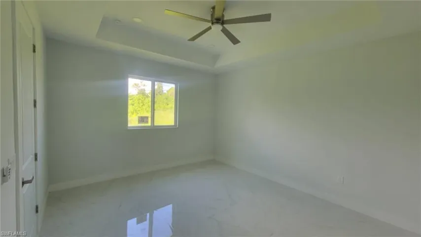 Empty room with ceiling fan and a tray ceiling