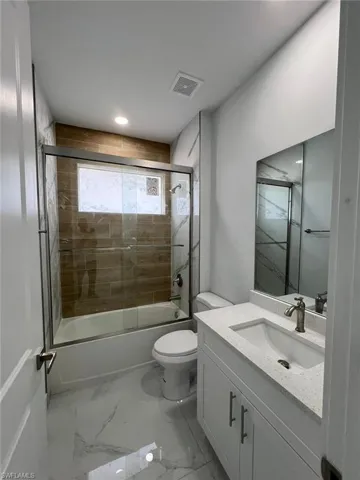 Full bathroom with combined bath / shower with glass door, tile patterned floors, toilet, and vanity