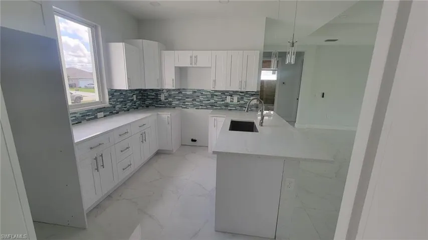 Kitchen featuring decorative backsplash, white cabinetry, sink, and light tile patterned floors