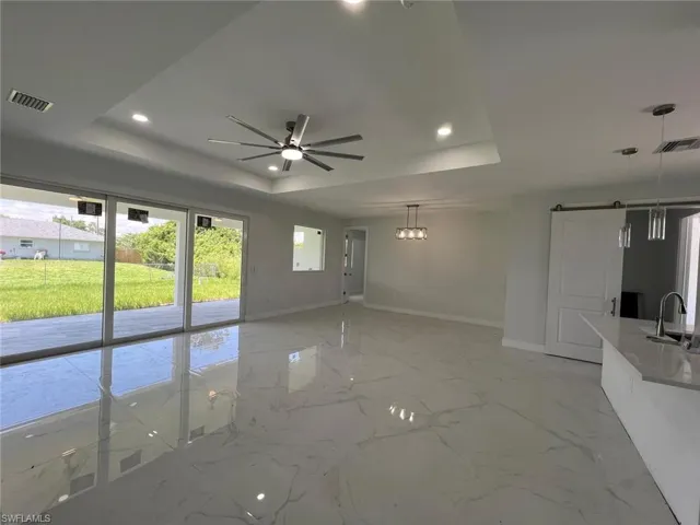 Tiled empty room with a raised ceiling, sink, and ceiling fan
