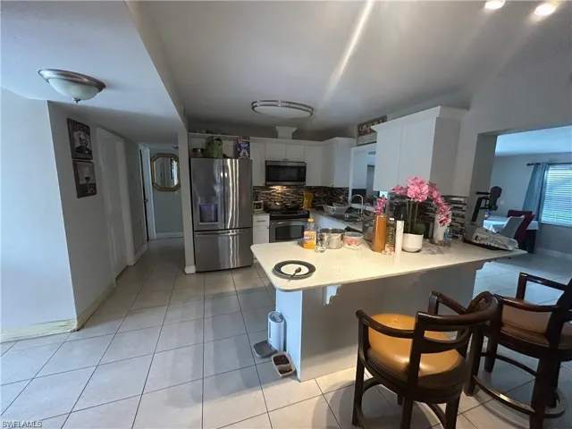 Kitchen featuring stainless steel appliances, decorative backsplash, white cabinets, and light tile patterned floors