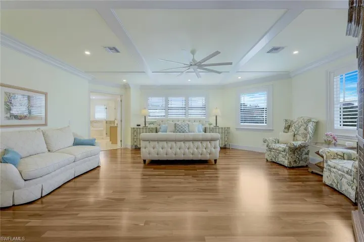 Bedroom featuring light wood-type flooring, beam ceiling, coffered ceiling, ceiling fan, and ornamental molding