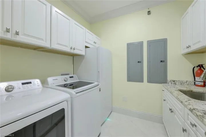 Laundry area featuring electric panel, ornamental molding, light tile patterned floors, cabinet space, and washing machine and clothes dryer