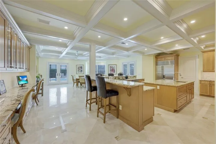 Kitchen featuring coffered ceiling, light stone counters, beamed ceiling, a breakfast bar, and french doors