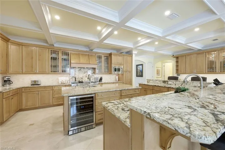 Kitchen with glass insert cabinets, beverage cooler, beamed ceiling, decorative backsplash, and light stone countertops