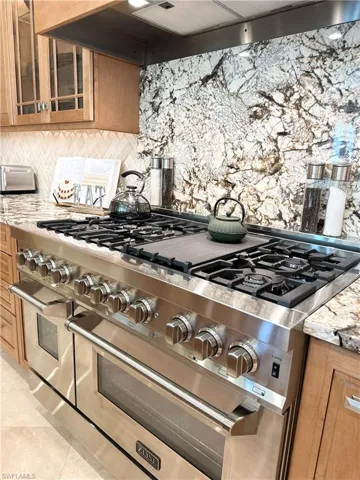 Kitchen view of custom range hood, light stone counters, brown cabinets, and double oven range
