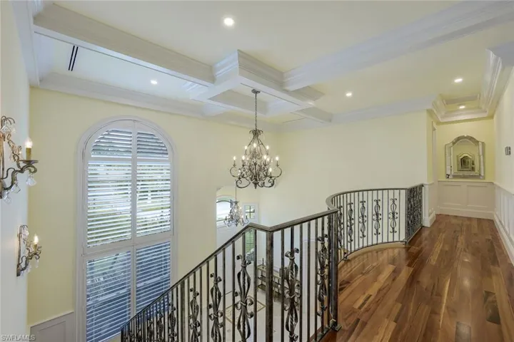Corridor featuring a chandelier, dark wood finished floors, an upstairs landing, a wainscoted wall, and beamed ceiling