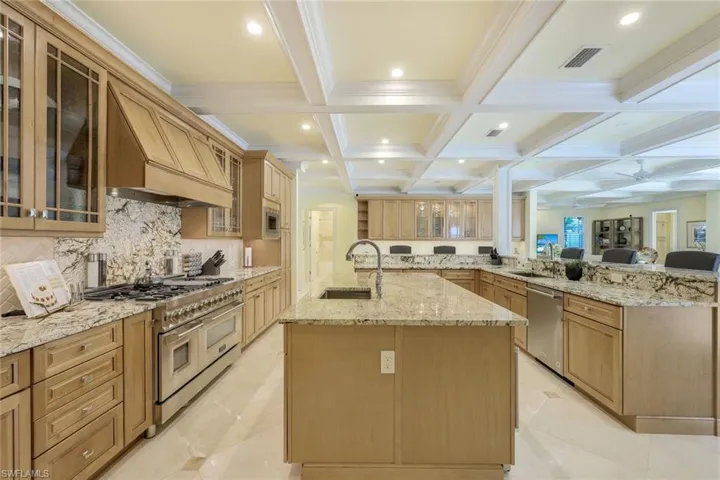 Kitchen featuring glass insert cabinets, beam ceiling, light stone countertops, stainless steel appliances, and coffered ceiling