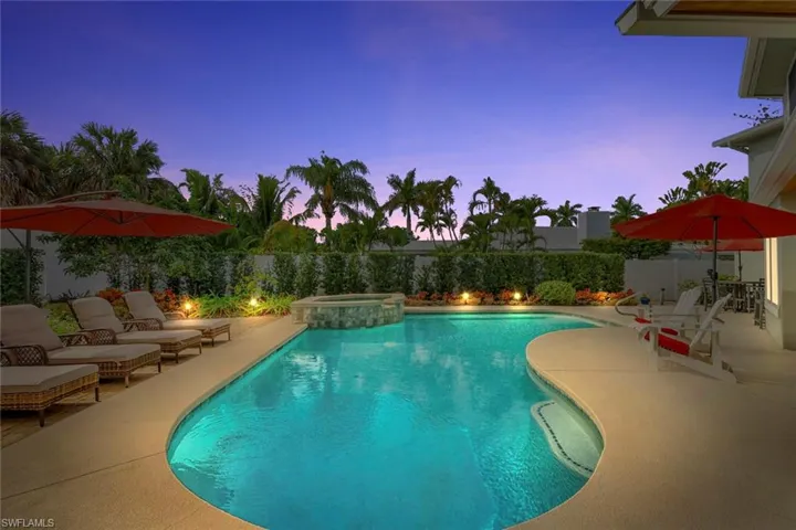 Pool at dusk with a patio area, a pool with connected hot tub, and a fenced backyard