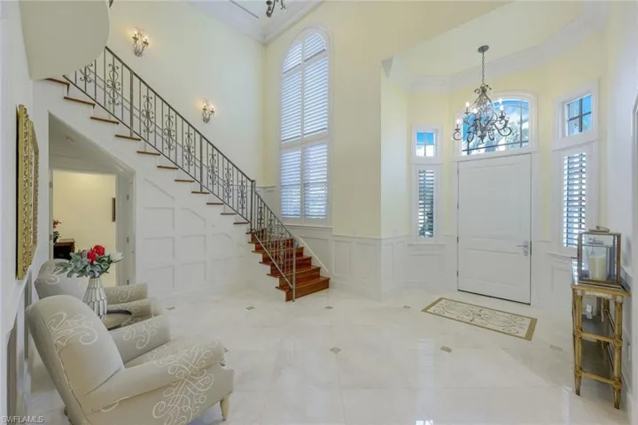 Foyer featuring a decorative wall, ornamental molding, a towering ceiling, stairway, and a wainscoted wall