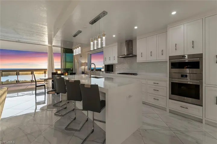 Kitchen featuring white cabinets, a breakfast bar, stainless steel double oven, hanging light fixtures, and light stone countertops