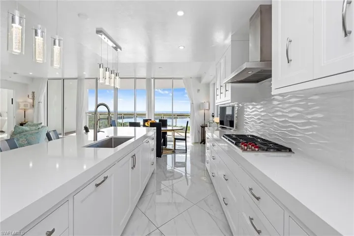 Kitchen featuring white cabinetry, pendant lighting, wall chimney range hood, backsplash, and expansive windows