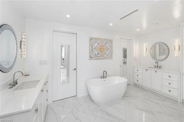 Full bath featuring two vanities, a freestanding tub, light marble finish floors, and recessed lighting