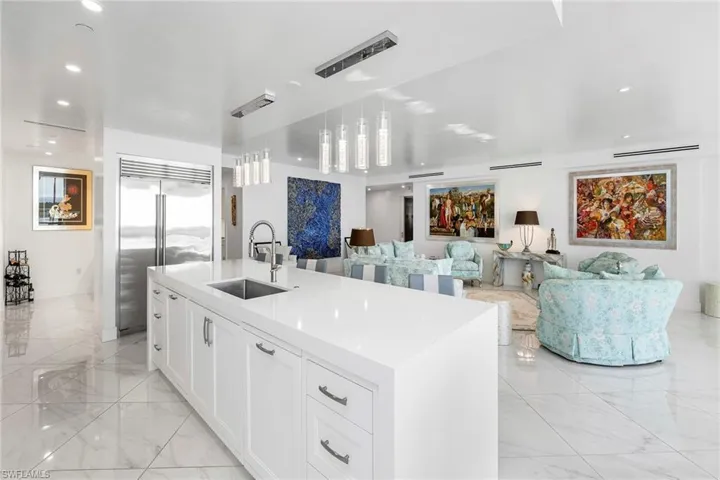 Kitchen with white cabinetry, stainless steel built in refrigerator, open floor plan, pendant lighting, and light stone countertops