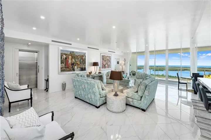 Living room featuring a water view, elevator, floor to ceiling windows, and light marble finish flooring