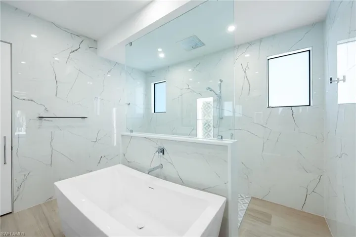 Bathroom featuring soaking tub, separate rain head shower, porcelain tile walls, and a healthy amount of sunlight