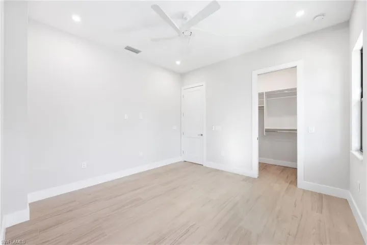 Unfurnished bedroom featuring a walk in closet, ceiling fan, a closet, and light hardwood / wood-style floors