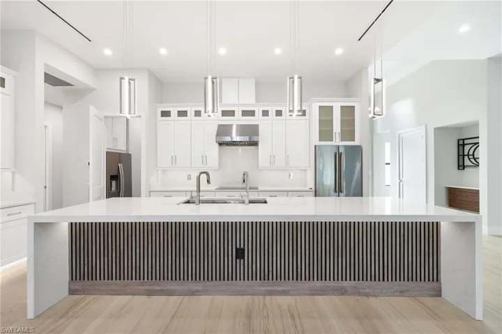 Kitchen with oversized island with dual faucets, waterfall quartz tops, wireless charging, custom built in wood, high end light fixtures and JennAir appliances with Butler pantry and additional refrigerator
