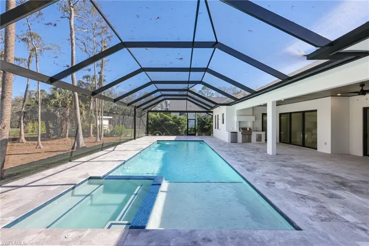 View of swimming pool with glass enclosure, ceiling fan, an in ground hot tub, a patio area, and exterior kitchen