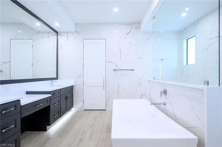 Bathroom with a soaking tub, vanity, wood-style tile floors, and porcelain tile walls