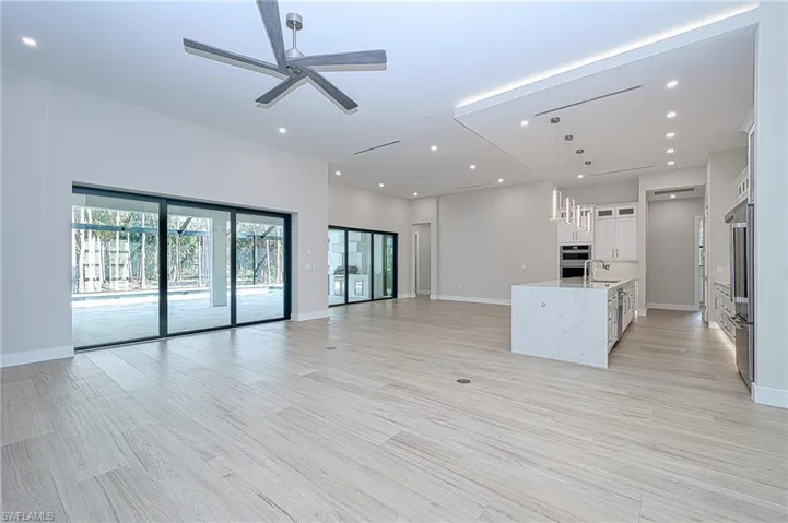Kitchen with ceiling fan, sink, light stone countertops, a large island with sink, and white cabinets