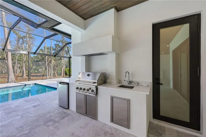 View of lanai with built in outdoor kitchen with propane grill from underground propane tank heating saltwater pool, grill, and pool/jacuzzi
