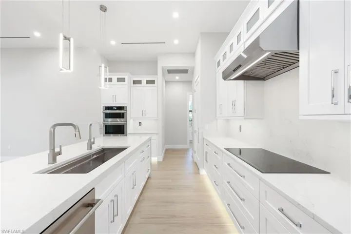 Kitchen featuring ventilation hood, sink, white cabinetry, and hanging light fixtures