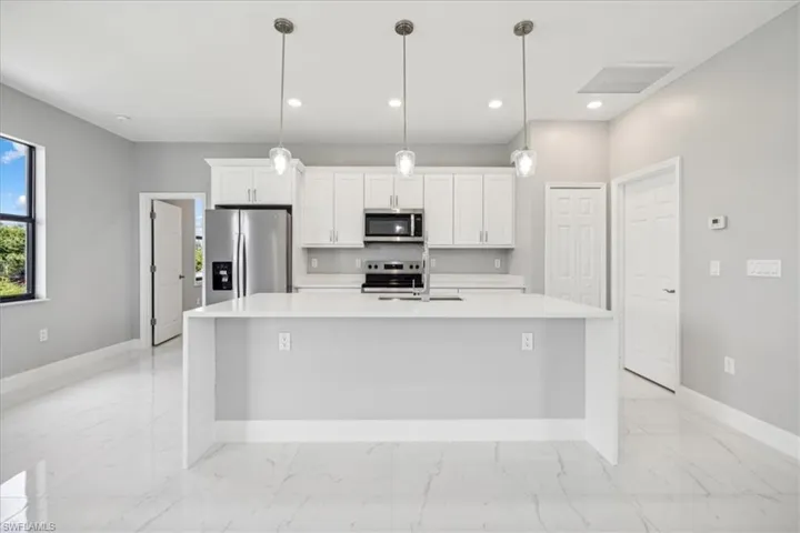Kitchen featuring appliances with stainless steel finishes, pendant lighting, a kitchen island with sink, and light tile patterned floors
