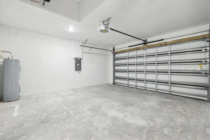 Garage featuring electric panel, a garage door opener, and water heater