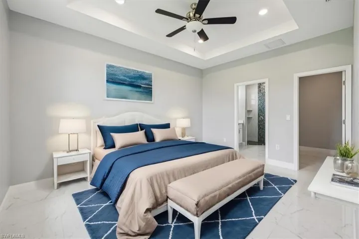Bedroom featuring ceiling fan, ensuite bathroom, tile patterned flooring, and a tray ceiling