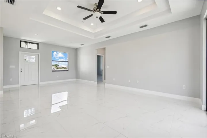 Tiled empty room with ceiling fan and a raised ceiling