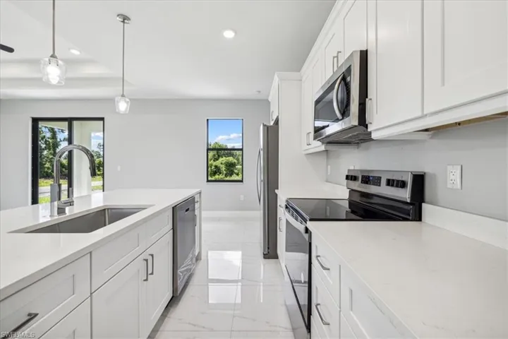 Kitchen with white cabinets, stainless steel appliances, light tile patterned flooring, and a wealth of natural light