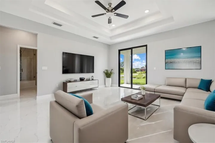 Living room featuring light tile patterned flooring, ceiling fan, and a tray ceiling
