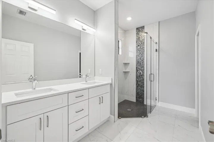 Bathroom featuring tile patterned floors, an enclosed shower, and dual bowl vanity