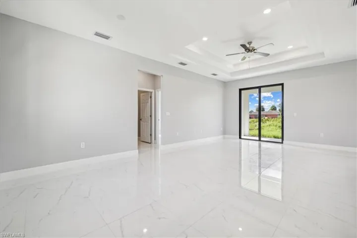 Tiled empty room with ceiling fan and a tray ceiling
