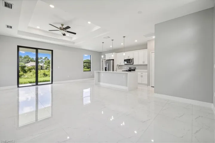Unfurnished living room with ceiling fan, sink, a tray ceiling, and light tile patterned floors