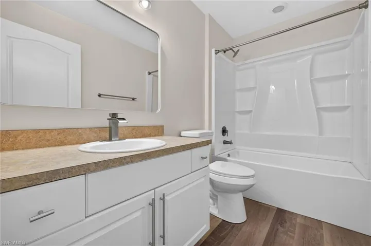 Bathroom featuring a white vanity with multiple cabinets, an oval sink, a light-toned countertop, and wood-finish flooring