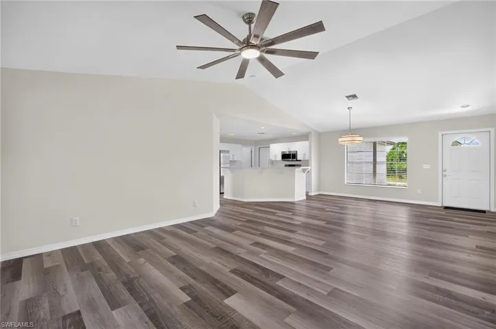 Vaulted ceiling with a ceiling fan, wood-finish flooring, white entry door with an arched window insert, and a pendant light fixture