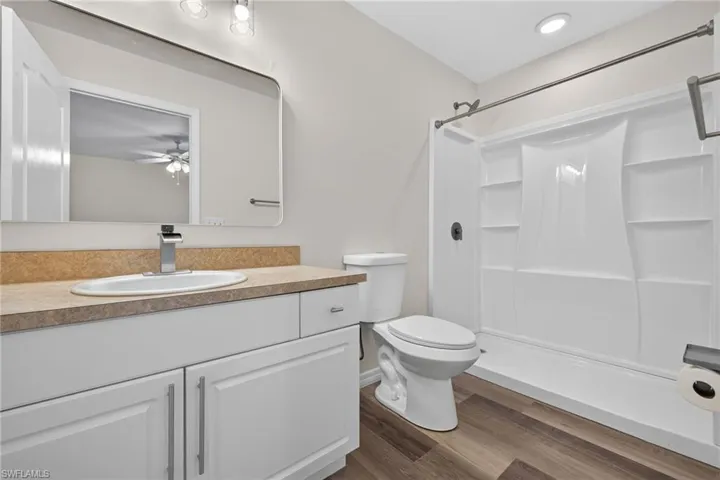 Contemporary bathroom featuring a white vanity with an undermount sink, a warm-toned countertop, a full-width mirror, a white shower and tub combination, and wood-finish flooring