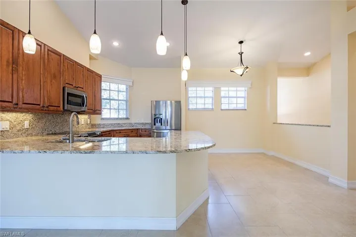 Kitchen featuring light stone countertops, sink, kitchen peninsula, decorative light fixtures, and appliances with stainless steel finishes