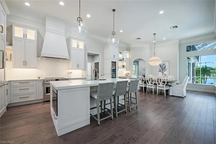 Kitchen with hanging light fixtures, white cabinets, custom range hood, high end stainless steel range, and dark wood-type flooring