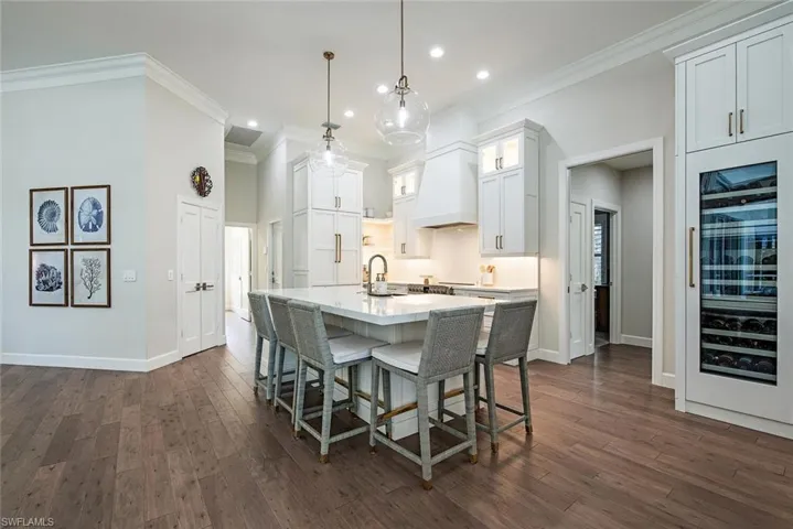 Kitchen featuring white cabinets, a center island with sink, custom exhaust hood, dark hardwood / wood-style flooring, and wine cooler