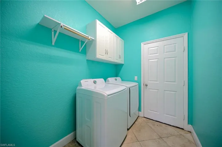 Clothes washing area featuring cabinets, light tile floors, and washing machine and clothes dryer