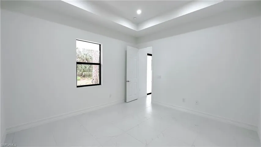 Unfurnished room featuring light marble finish floors and a tray ceiling
