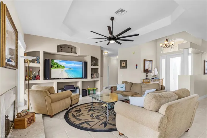 Living room with built in shelves, a tray ceiling, a ceiling fan, a fireplace, and light tile patterned floors