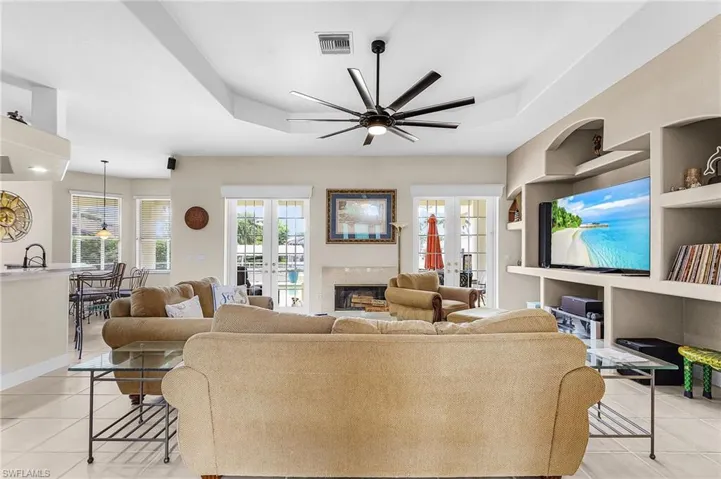 Living room with light tile patterned floors, built in features, a glass covered fireplace, and a ceiling fan